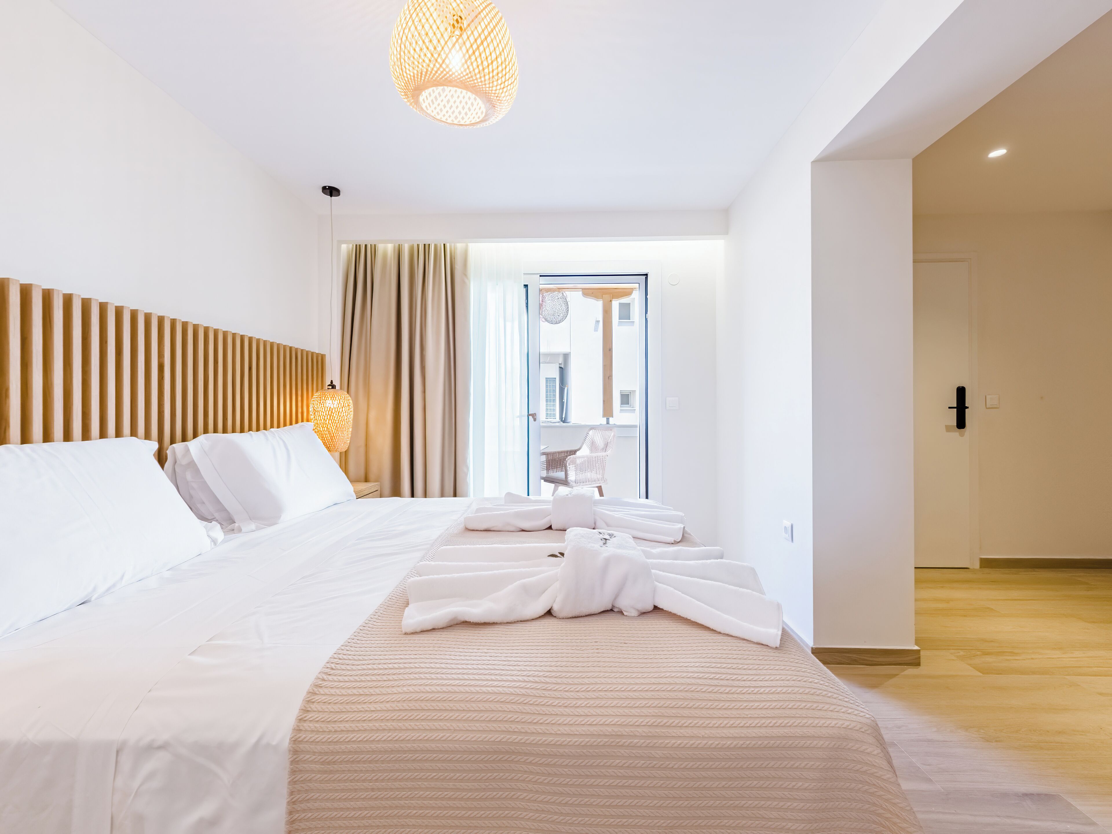 A modern hotel room with a large bed, a wooden headboard, a bedside lamp, and a view of the city through the window.