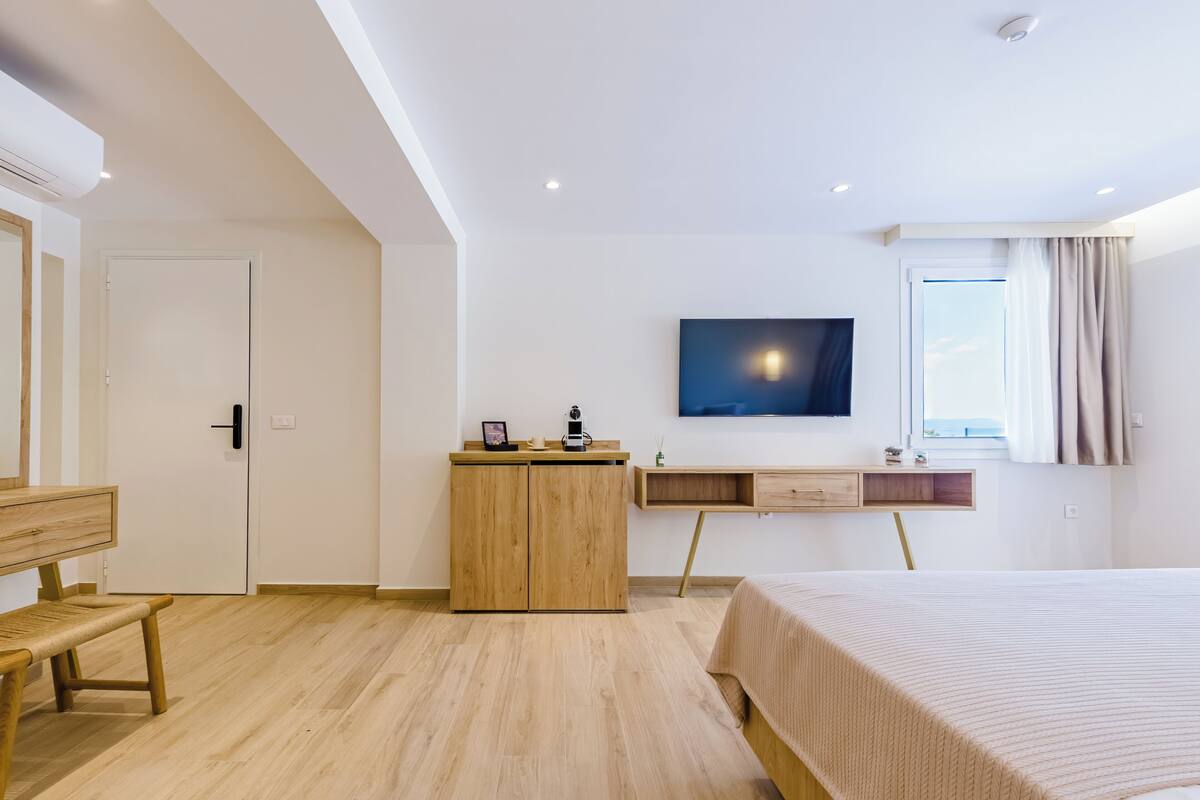 A modern bedroom with a wooden bed, a desk, a chair, and a TV mounted on the wall.