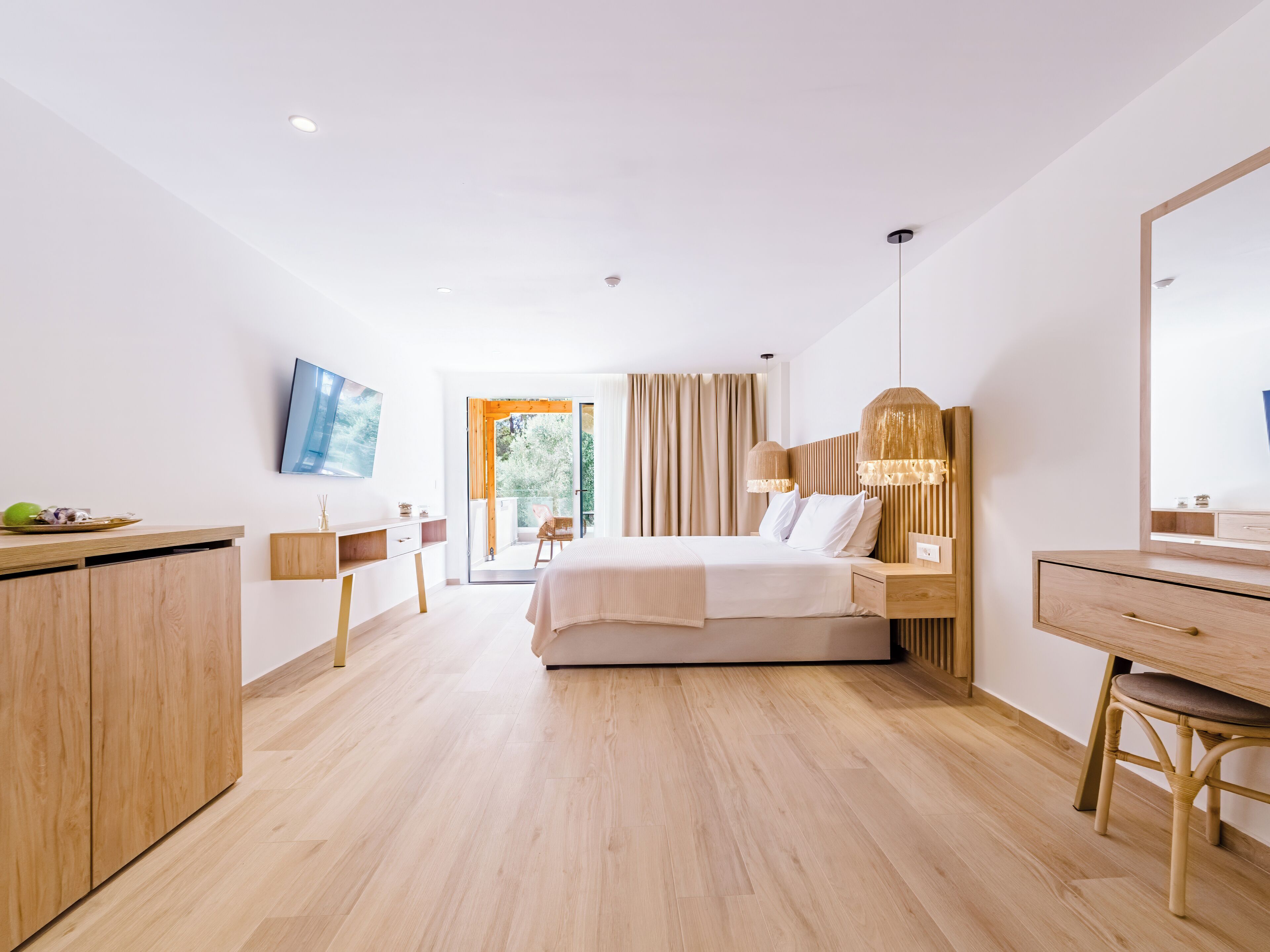Habitación de hotel con cama, escritorio, silla, cómoda y televisor montado en la pared.