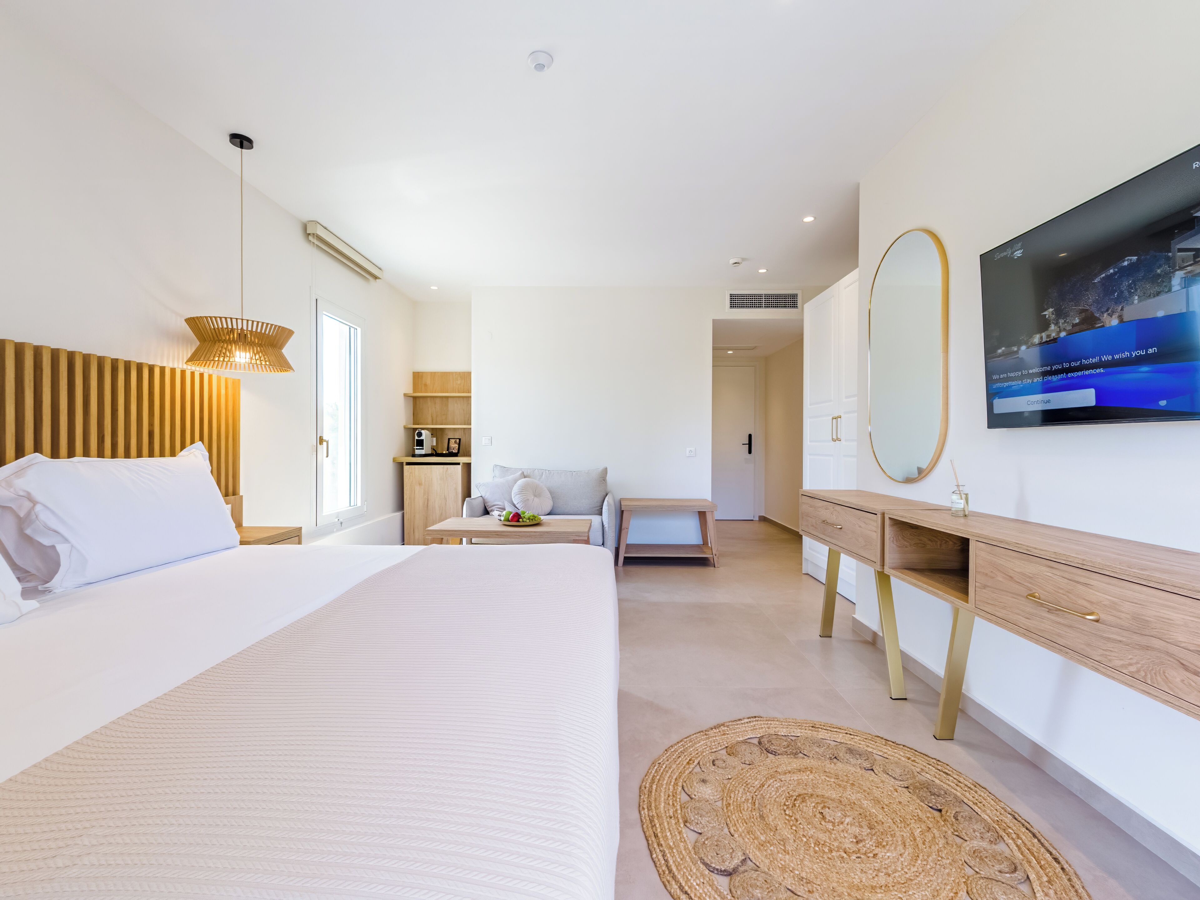 Habitación de hotel moderna con una cama grande, una mesita de noche, un sofá, un televisor y un espejo.