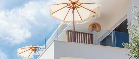 A modern building with balconies, outdoor umbrellas, and a clear sky.