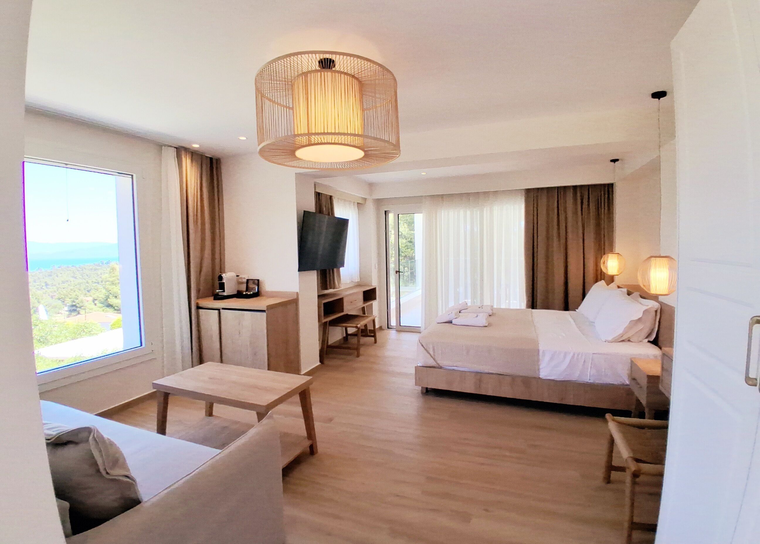 A hotel room with a bed, a desk, a TV, and a large window offering a view.