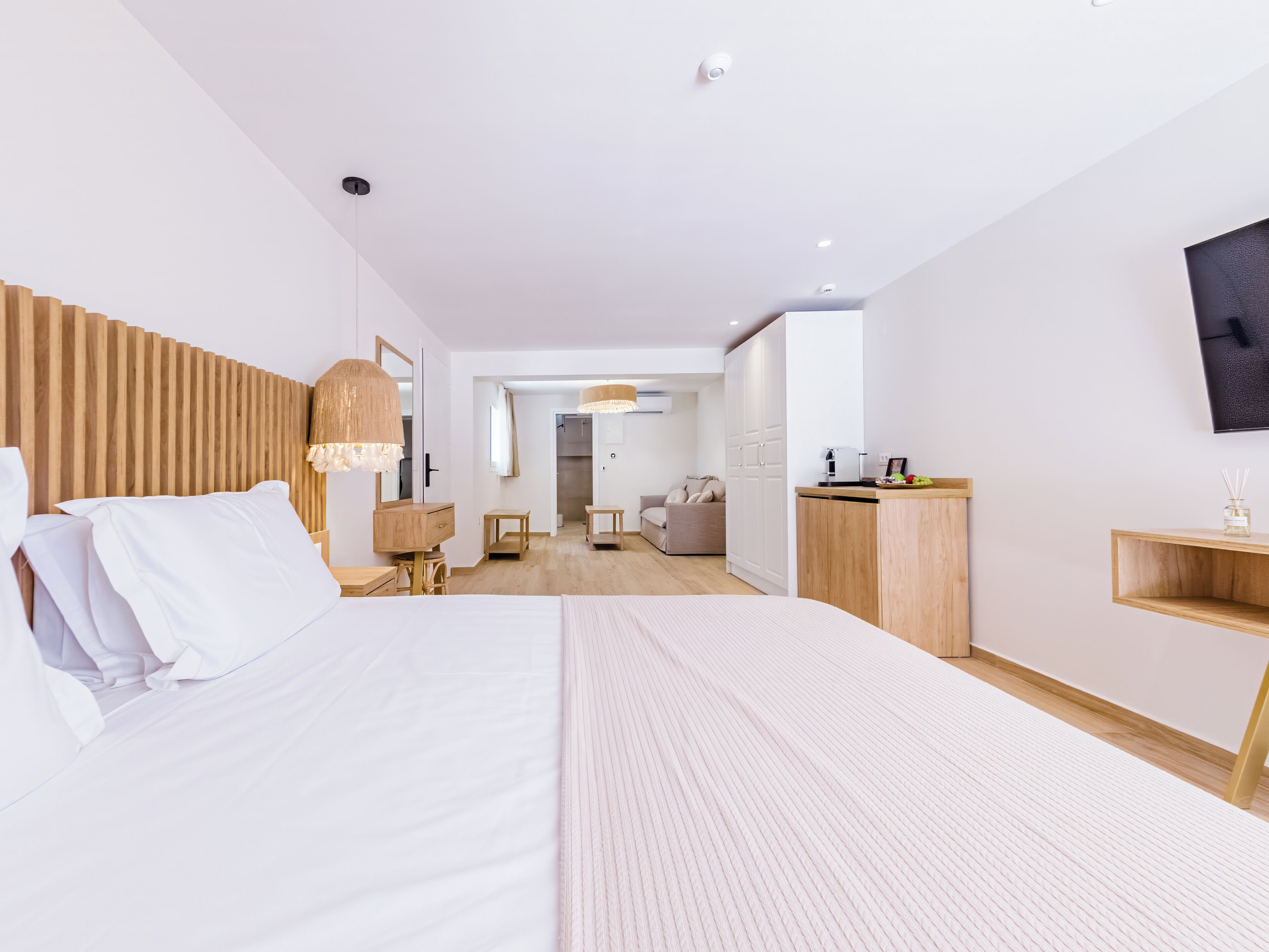 A modern hotel room with a large bed, wooden headboard, a desk, and a wardrobe.