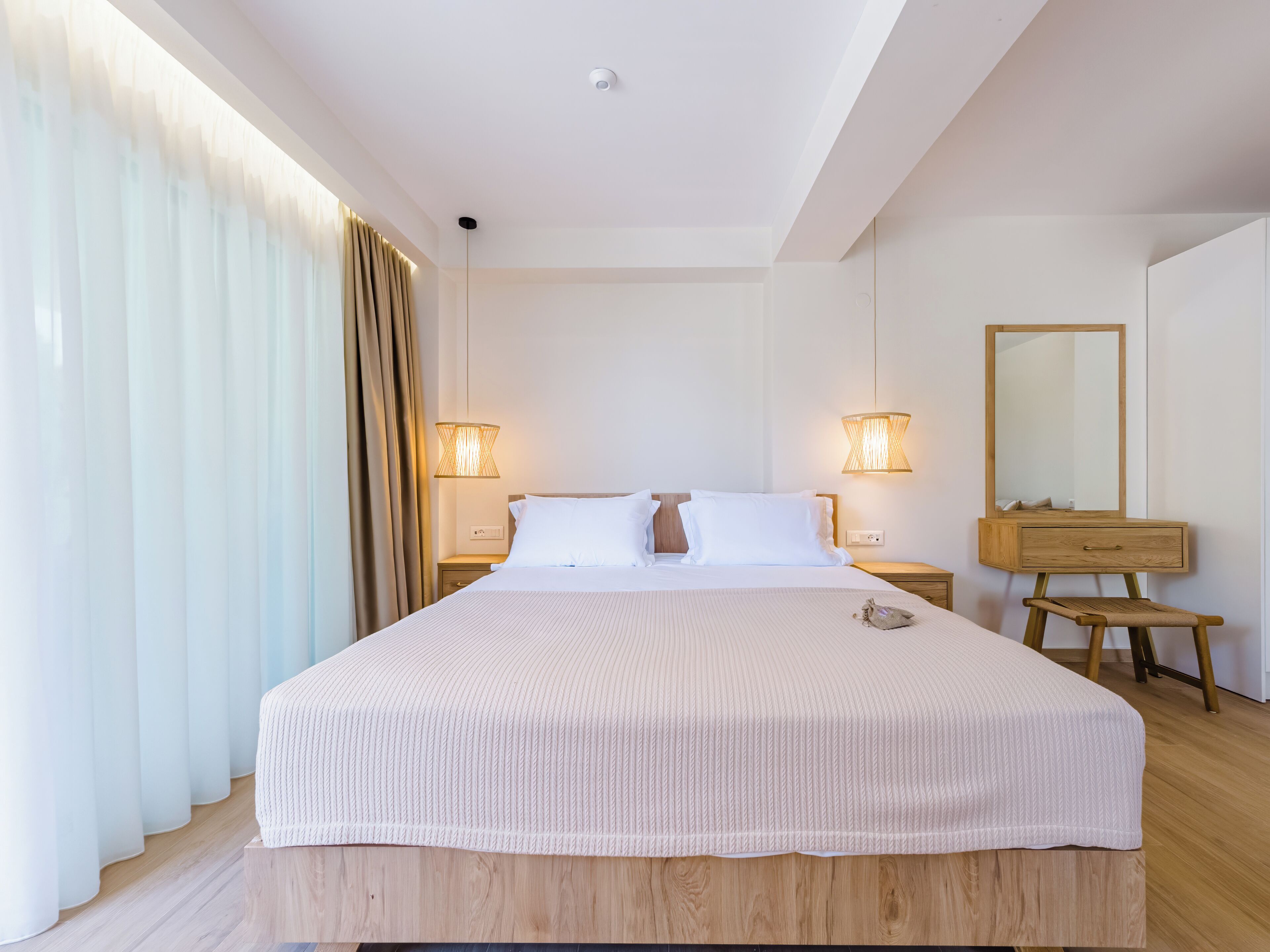A modern hotel room with a large bed, wooden headboard, bedside lamps, a wooden dresser, and a mirror.