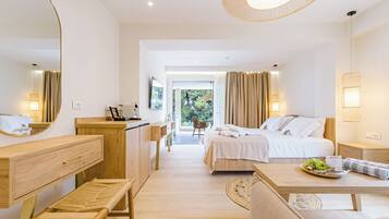 Una habitación de hotel moderna con un escritorio de madera, una cama con ropa blanca, un banco y una mesa de comedor con un plato de fruta.