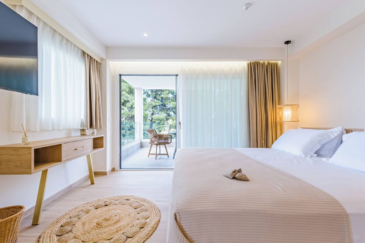 A modern hotel room with a large bed, a desk, a TV, and a balcony with a chair.