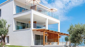 Una casa moderna de dos pisos con un balcón, una pérgola de madera y un cielo azul despejado.