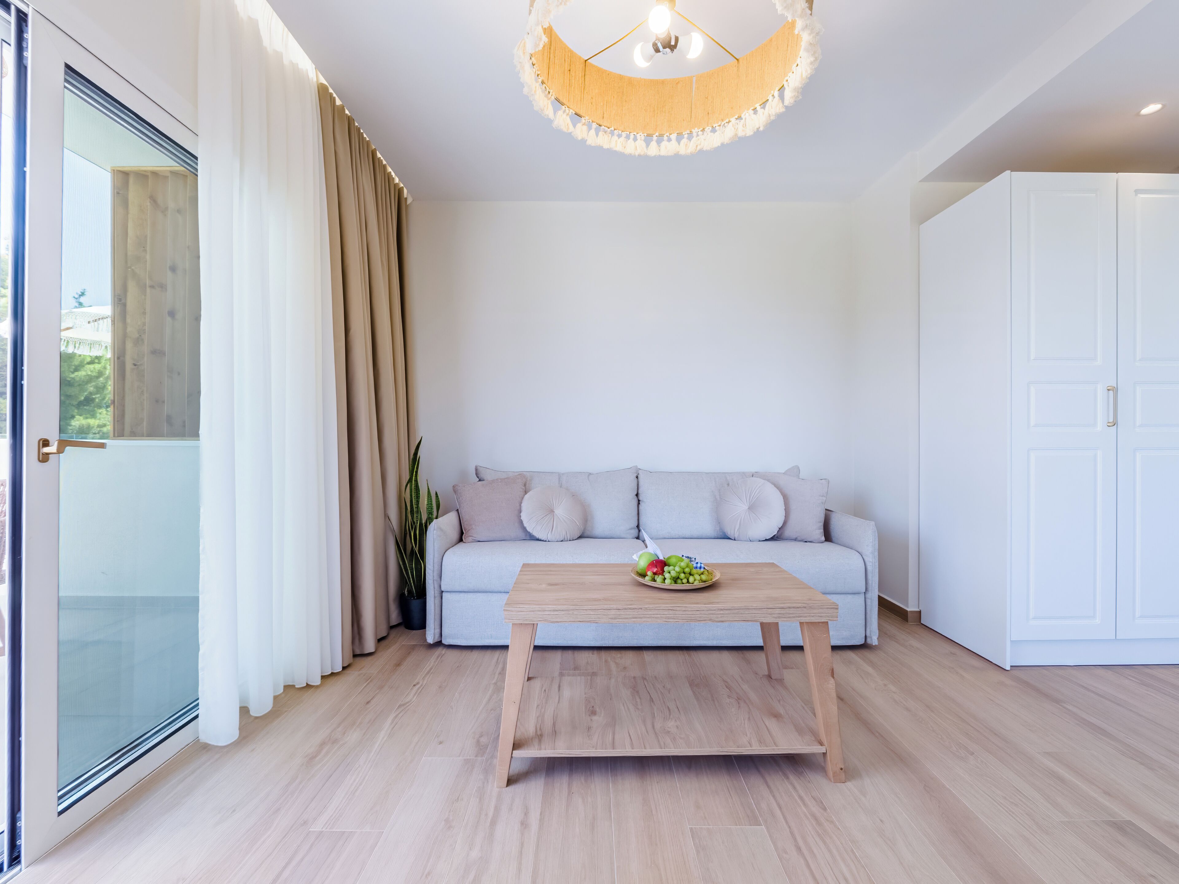 Una sala moderna con un sofá de color gris claro, una mesa de centro de madera y un armario blanco.