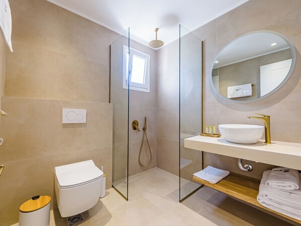 A modern bathroom with a glass-enclosed shower, a white toilet, a sink with a gold faucet, and a mirror above the sink. - Serenity Hill (Kassandra)