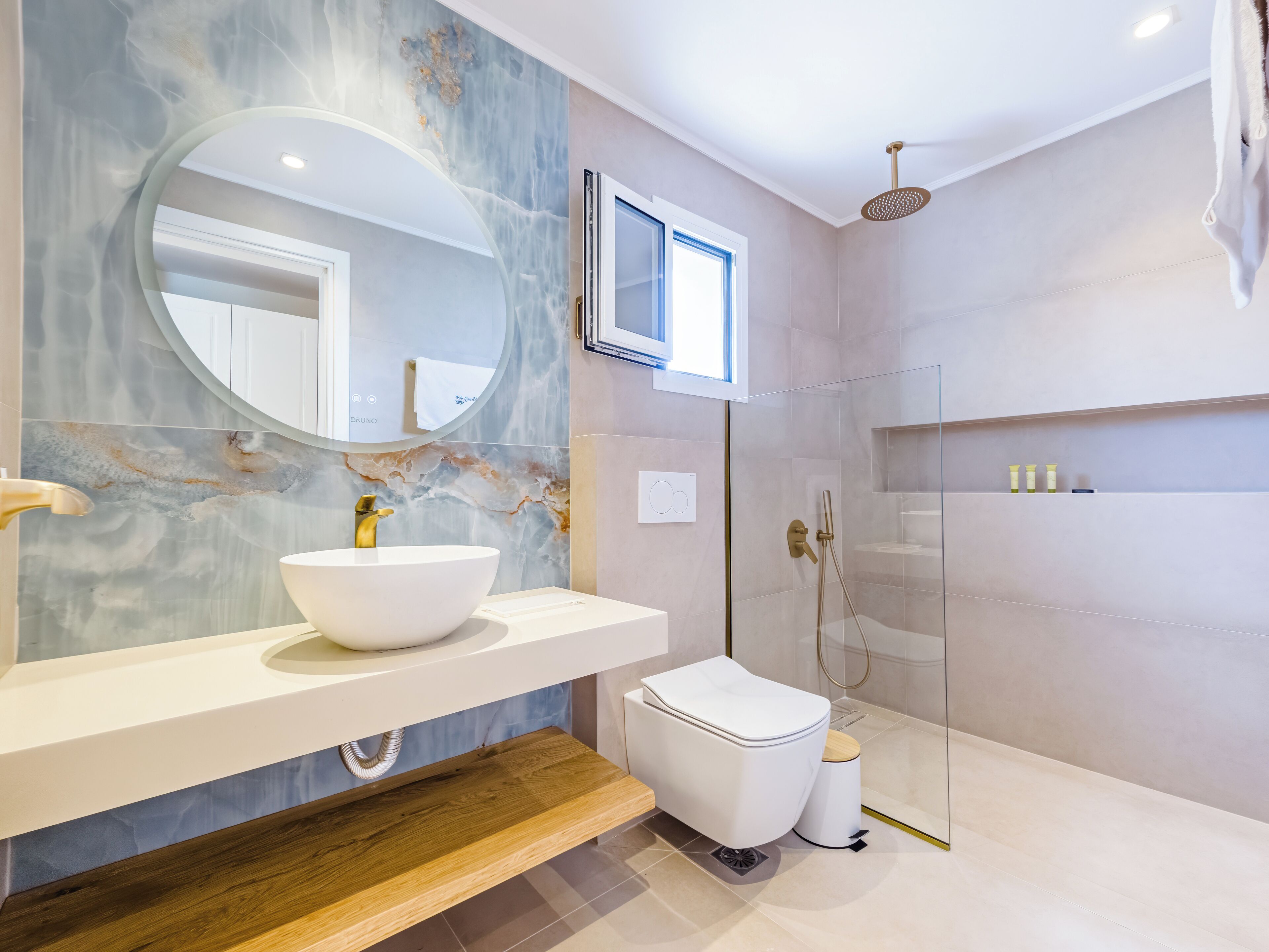A modern bathroom with a marble vanity, a toilet, a shower enclosure, and a mirror.