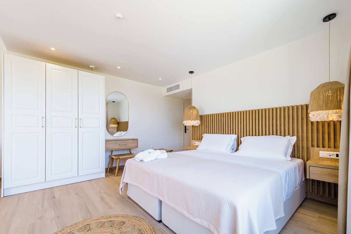 A modern bedroom with a large bed, a dresser, a mirror, and a wardrobe.