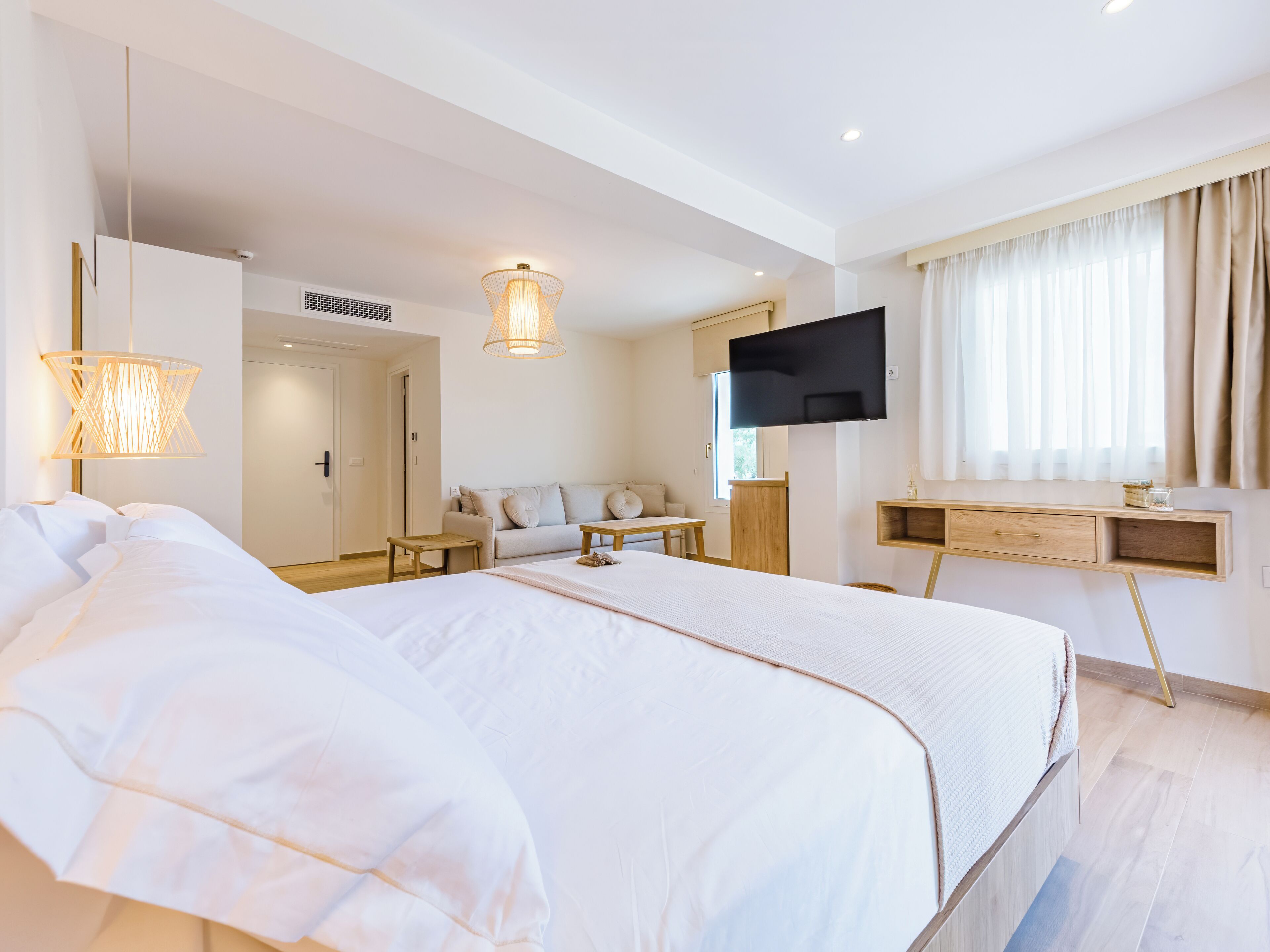 A modern hotel room with a large bed, a TV mounted on the wall, and a desk with a chair.