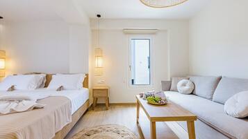 Une chambre d’hôtel moderne, équipée d’un lit, d’un canapé, d’une petite table avec des fruits, d’un tapis tissé et d’une fenêtre donnant sur un paysage agréable.