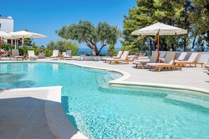 A pool area with lounge chairs and umbrellas, surrounded by trees and a view of the sea. - Serenity Hill (Kassandra)