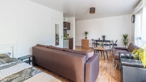 Een moderne woonkamer met een bruine bank, een zwarte leren bank en een eethoek met een tafel en stoelen.