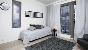 Et moderne soveværelse med en seng, et sengebord med lampe, et stort vindue med gardiner og et vægur.