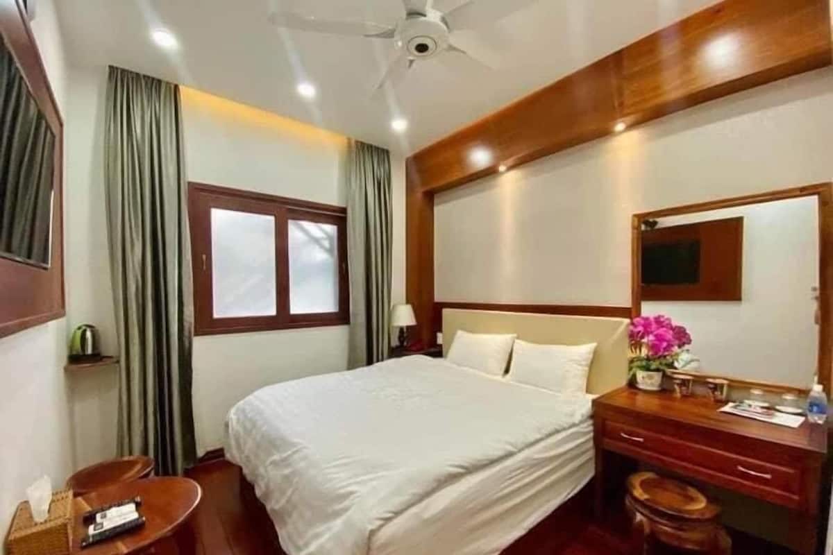 A hotel room with a bed, a desk, a chair, a mirror, and a ceiling fan.