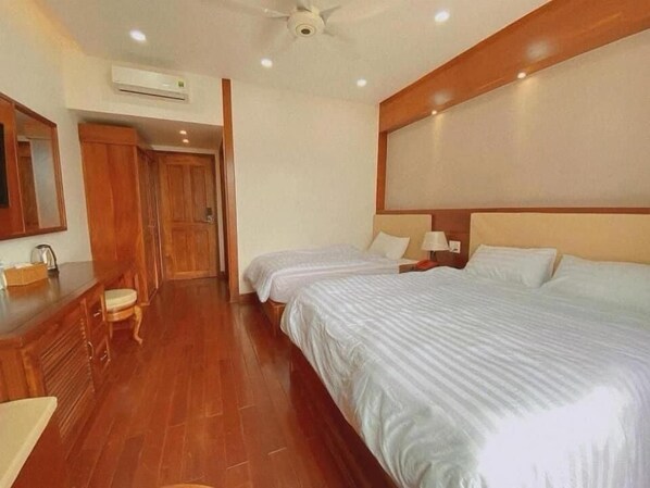 A hotel room with a wooden floor, two beds with white bedding, a wooden headboard, a nightstand with a lamp, a mirror, and an air conditioning unit. - Pandora Hotel CT by Bay Luxury (Can Tho)