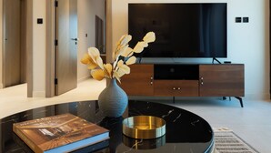 A modern living room with a large flat-screen TV, a dark marble coffee table, a decorative vase with dried flowers, and a book titled "Decoration Design". - Spacious 2BR Canal View - Heart of B Bay (Dubai)