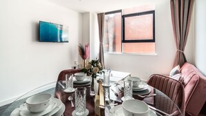 Un coin repas avec une table en verre pour quatre personnes, un téléviseur fixé au mur et une fenêtre avec des rideaux.