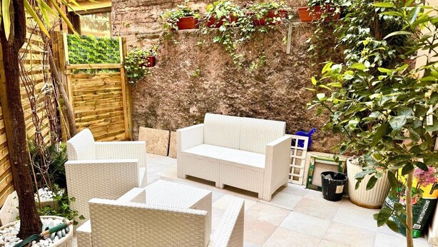 Ein Patio mit Korbmöbeln, einer Steinwand und Topfpflanzen.