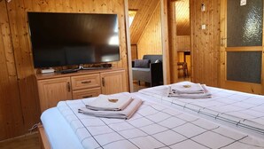 A room with two beds, a television, wooden walls, and a small seating area. - Villa Nova Hévíz - Apartment 7 top floor (Hévíz)