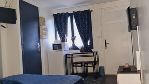 Et lille værelse med en seng, et lille bord med mikroovn, et TV ophængt på væggen og en dør med håndtag.
