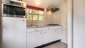 Eine moderne Küche mit weißen Schränken, einem Edelstahlbackofen, einem Fenster mit rotem Vorhang und einem Gasherd.