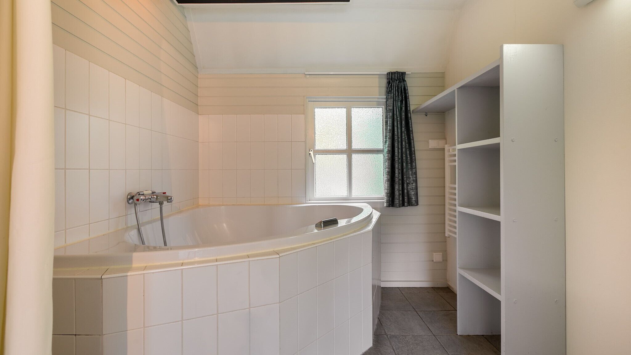 A bathroom with a freestanding bathtub, a window with frosted glass, and built-in shelving.