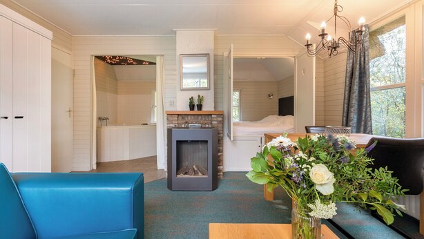 Ein modernes Wohnzimmer mit Kamin, einem Essbereich mit Blumenvase und Blick ins Freie durch ein Fenster.
