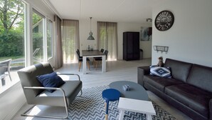 A modern living room with a sofa, a coffee table, and a dining area with a table and chairs. - Holiday villa for 4 persons (Steendam)