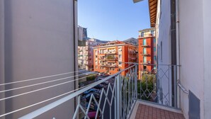 Un balcón con baranda de metal que da a una calle con coches aparcados y edificios al fondo.