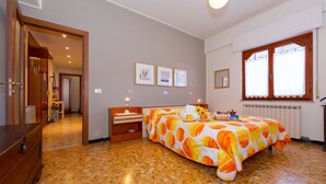 Un dormitorio con cama, cómoda, mesita de noche, ventana con cortinas y radiador.