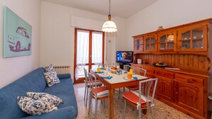 Un comedor con una mesa dispuesta para cuatro, un sofá azul con cojines estampados, un aparador de madera con puertas de cristal y un televisor sobre un mueble.