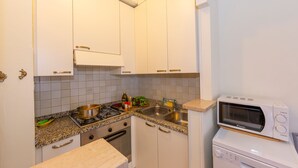 Cocina compacta con armarios blancos, encimera de granito, estufa, pileta y microondas integrado.