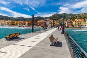 A waterfront promenade with benches, a railing, and colorful buildings in the background. - Bluemind Apartment in Alassio (Alassio)