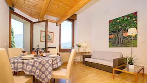 A dining area with a table set for two, a sofa, and a painting on the wall.