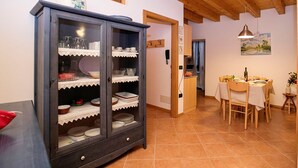 Uma área de refeições com mesa e cadeiras de madeira, um armário com portas de vidro e uma cozinha ao fundo.