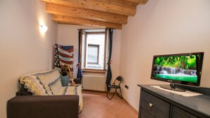Uma sala de estar acolhedora com um sofá, uma televisão, uma janela com cortinas e um radiador.