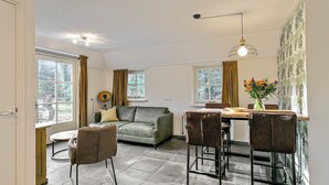 A modern living room with a sofa, a dining table with chairs, and a vase of flowers. - Ground-floor bungalow for 4 people (Herpen)