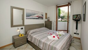 A bedroom with a bed, a nightstand, a lamp, a TV, and a window with a view of trees. - Appartamento Lara in Riva del Garda (Riva del Garda)