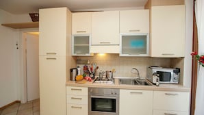 A compact kitchen with white cabinets, a stainless steel oven, a microwave, and a sink. - Appartamento Lara in Riva del Garda (Riva del Garda)