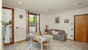 A dining area with a table set for four, a sofa, and a door to the right. - Appartamento Lara in Riva del Garda (Riva del Garda)