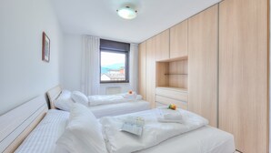A hotel room with two beds, a large window with a view, and a wooden wardrobe. - Appartamento Amy in Riva del Garda (Riva del Garda)