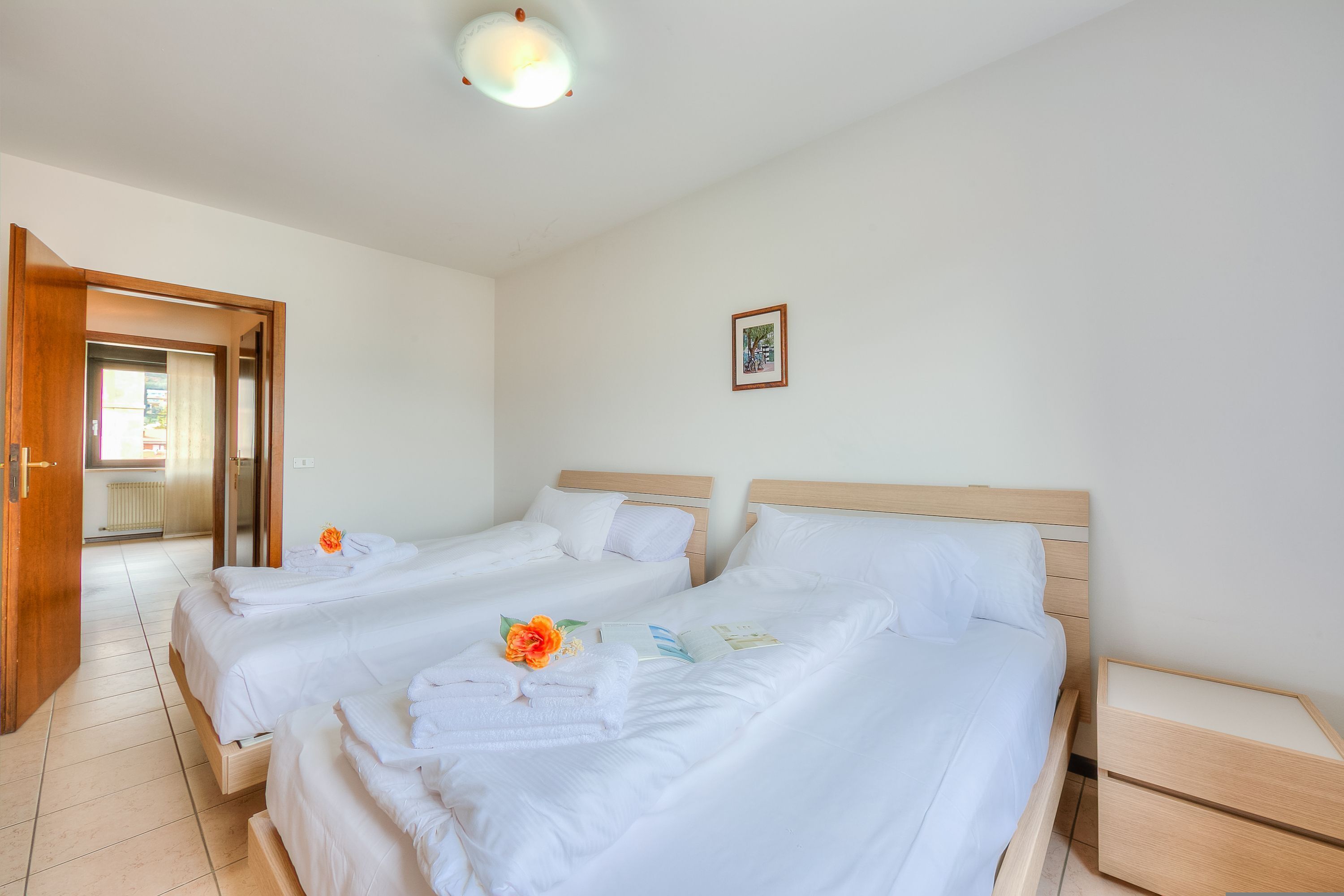 A hotel room with two beds, a wooden headboard, a bedside table, and a framed picture on the wall.