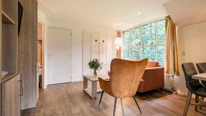 Ein modernes Zimmer mit Holzboden, einem braunen Ledersessel, einem Holztisch, einer Couch und einem Fenster mit Vorhängen.