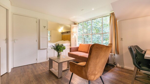 Ein modernes Zimmer mit Holzboden, einem braunen Ledersessel, einem kleinen Tisch mit einer Vase und einem Fenster mit Vorhängen.