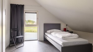 Una camera da letto con un letto, una sedia, un comodino, una lampada e vista su un paesaggio verde attraverso una finestra.