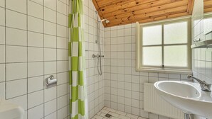 Une salle de bain avec des murs recouverts de carreaux blancs, un rideau de douche à rayures vertes et blanches, un plafond en bois, une fenêtre et un lavabo blanc avec un miroir.