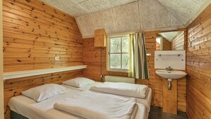 Une chambre de style cabane avec deux lits, une fenêtre avec des rideaux, un lavabo et un miroir.
